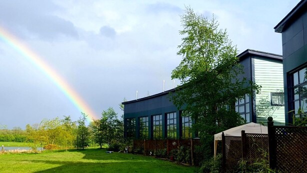 A modern building with large windows, a grassy yard, and a pond. - 59 Riverun (Belturbet)