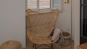 A room with a large window overlooking a beach, a wicker chair, a floor lamp, and a small table.