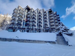 A multi-story hotel with balconies, a snow-covered entrance, and a staircase leading up to the building.
