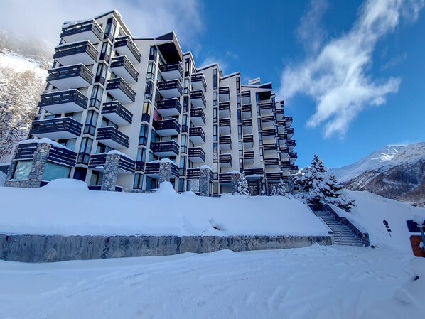 A multi-story hotel with balconies, a stone facade, and a snowy landscape in the background.