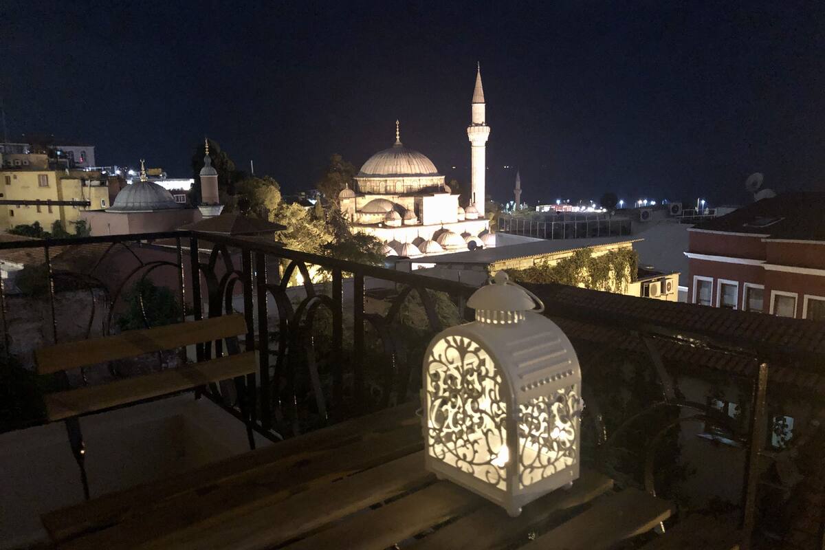 Vista noturna de uma mesquita com um minarete, uma cúpula e um lanternário numa varanda.