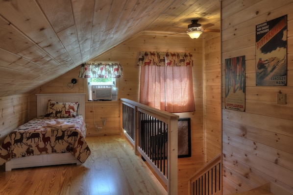 A cozy cabin room with a bed, a window with curtains, an air conditioning unit, and a staircase.