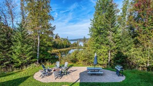 A patio area with outdoor furniture and a grill, surrounded by trees and a view of a lake. - 🐾28 Bunker Ave - Shared waterfront and access to Rangeley Lake, dog friendly (Rangeley)