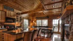 A rustic cabin interior with wooden walls, a kitchen area with a stove, microwave, and bar seating. - 🐾28 Bunker Ave - Shared waterfront and access to Rangeley Lake, dog friendly (Rangeley)