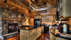 A spacious kitchen with a stone fireplace, wooden cabinets, and a central island. - 🐾28 Bunker Ave - Shared waterfront and access to Rangeley Lake, dog friendly (Rangeley)