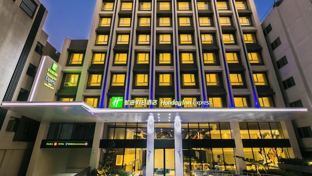 Un hôtel à plusieurs étages doté d’une façade moderne, de fenêtres illuminées et d’une entrée imposante surmontée d’un auvent en verre.