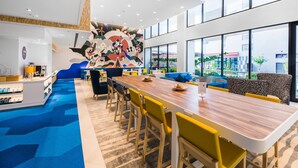 Un hall d’hôtel moderne avec un long comptoir d’accueil en bois, des chaises jaunes et une fresque colorée sur le mur.