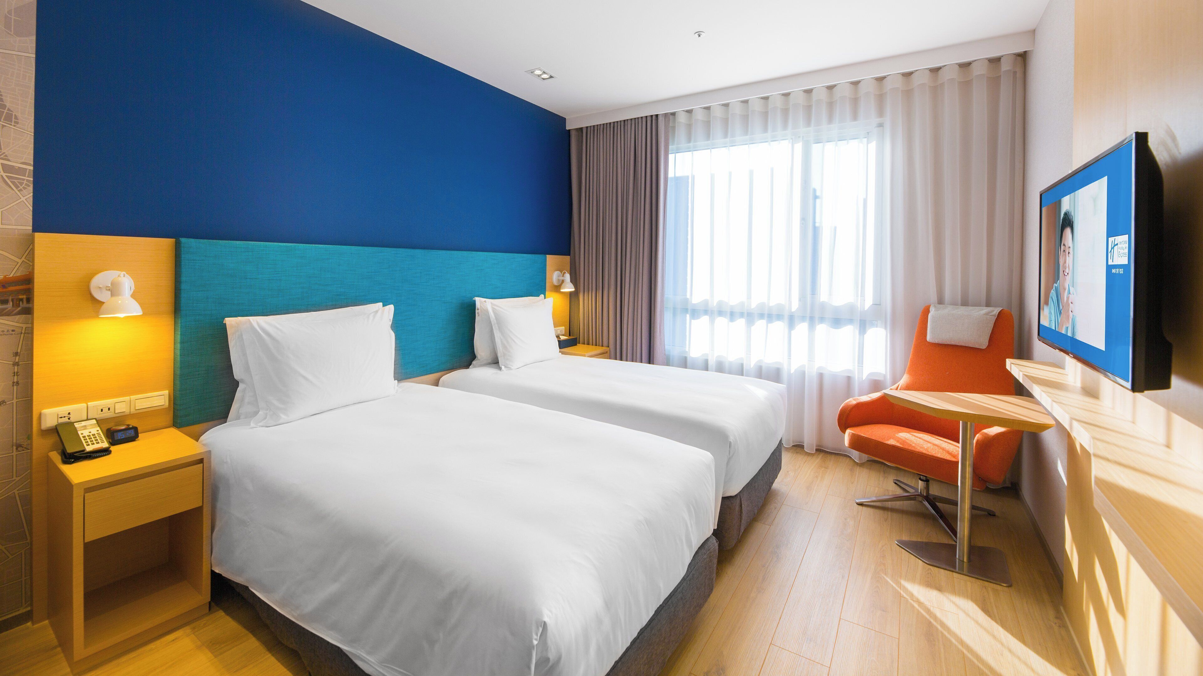 A hotel room with two beds, a television, a desk, and a chair.