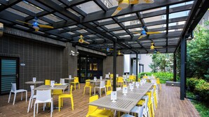 Un café en plein air avec des tables et des chaises, un plancher en bois et un espace couvert doté de ventilateurs de plafond.