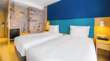 A hotel room with a large bed, a desk, a chair, a map on the wall, and a nightstand with a lamp.