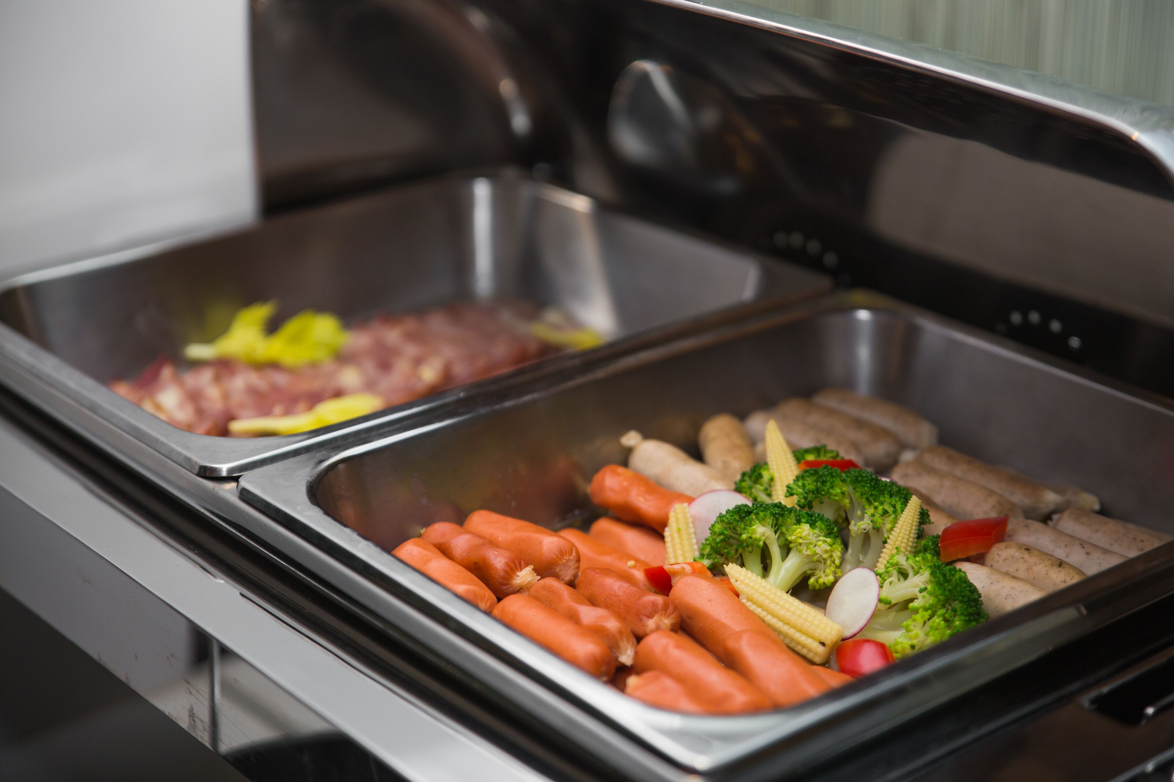 A buffet with various food items including sausages, vegetables, and meat.