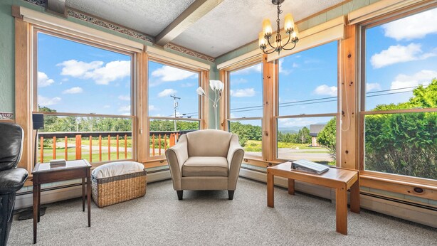 A cozy room with a large window, a comfortable chair, a small table, and a wicker basket. - 🐾Dallas Ridge - Dog friendly four seasons home in Rangeley! (Rangeley)