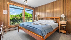 A bedroom with a wooden bed, two bedside tables, a large window, and a view of greenery. - 🐾Dallas Ridge - Dog friendly four seasons home in Rangeley! (Rangeley)