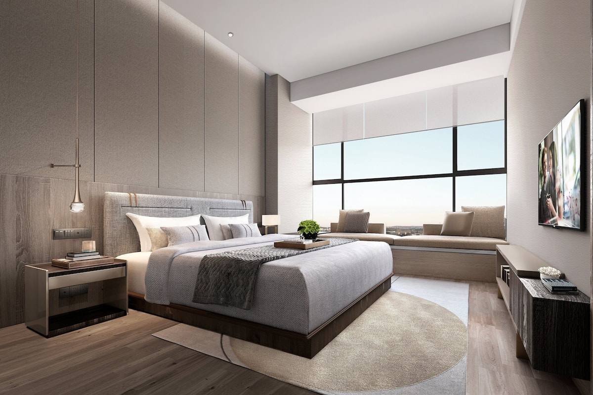 Quarto moderno com uma cama grande, mesas de cabeceira, luminária pendente, janela ampla e televisão.