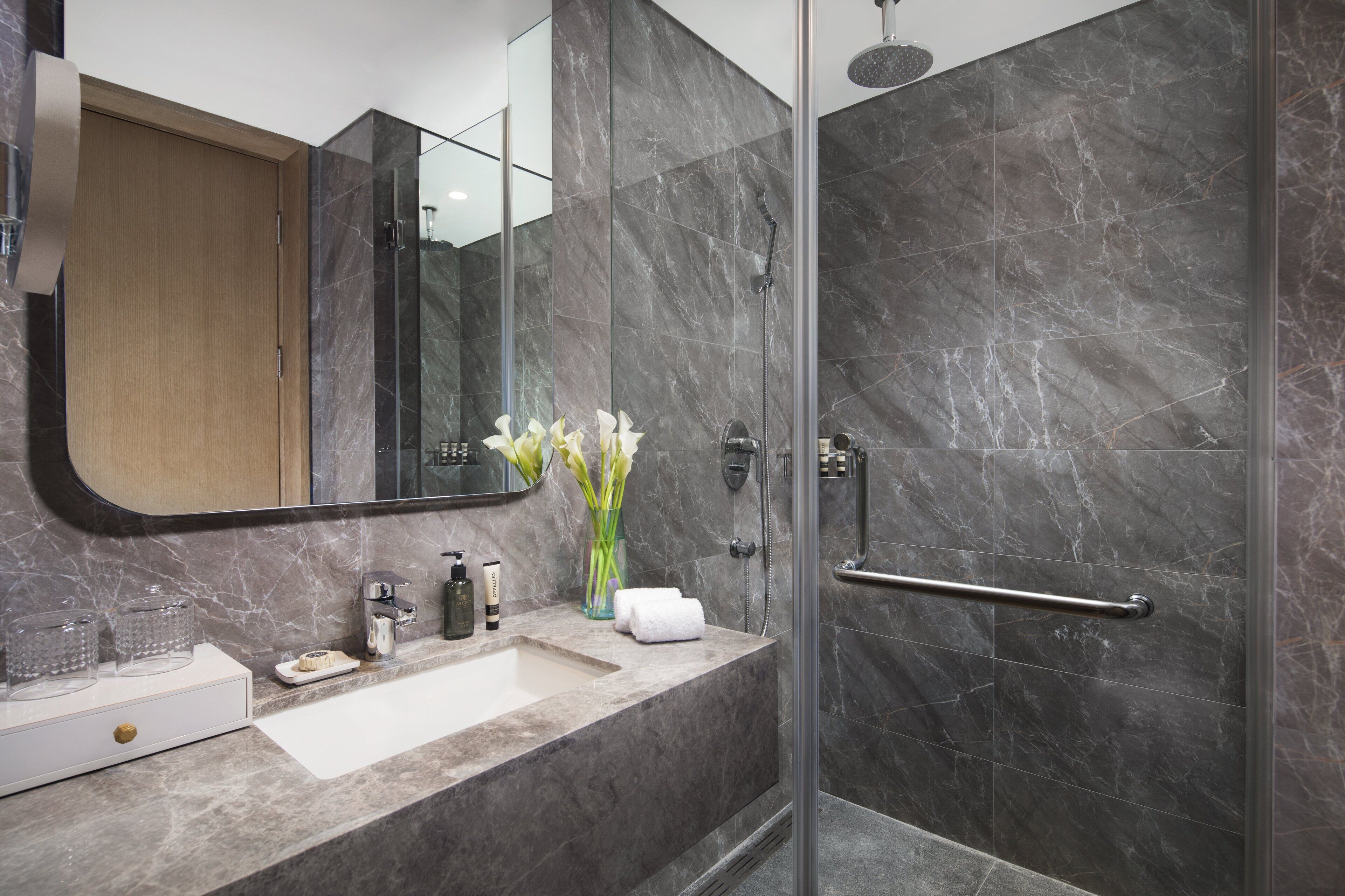 Un baño moderno con lavamanos de mármol, cabina de ducha de vidrio y tocador de madera.