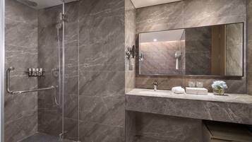 Une salle de bain moderne avec une douche à parois de verre, un mur recouvert de carreaux de marbre, un grand miroir et un meuble-lavabo avec des articles de toilette.