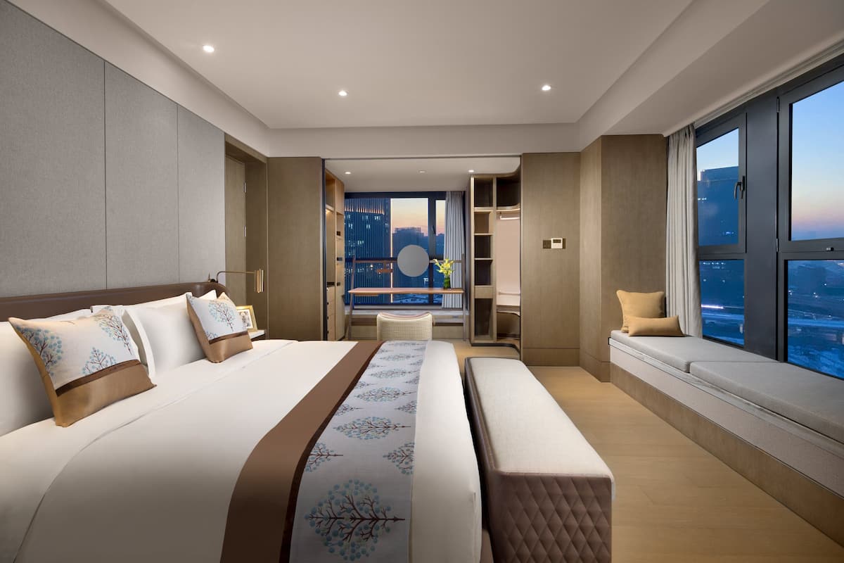 Quarto de hotel moderno com uma cama grande, área de estar com vista e varanda com vista para a cidade.