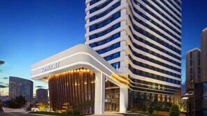 Un hôtel moderne avec une entrée incurvée, une enseigne bien visible et une vue sur le paysage urbain en arrière-plan.