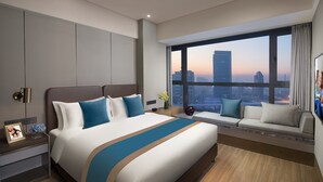 Une chambre d’hôtel moderne avec un grand lit, un canapé près de la fenêtre et une vue sur la ville.