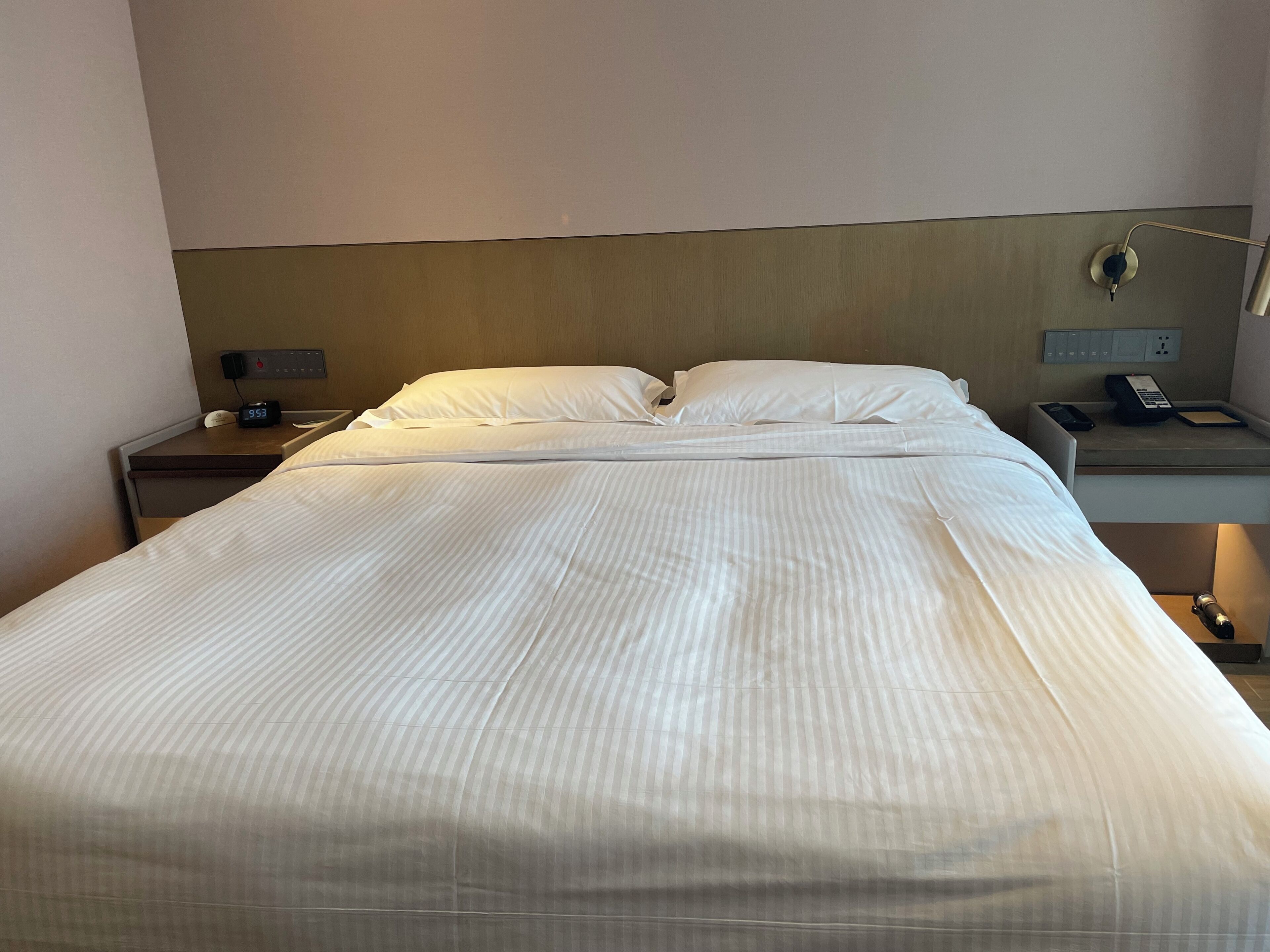 A neatly made bed in a hotel room with a headboard, bedside tables, a clock, and a phone.