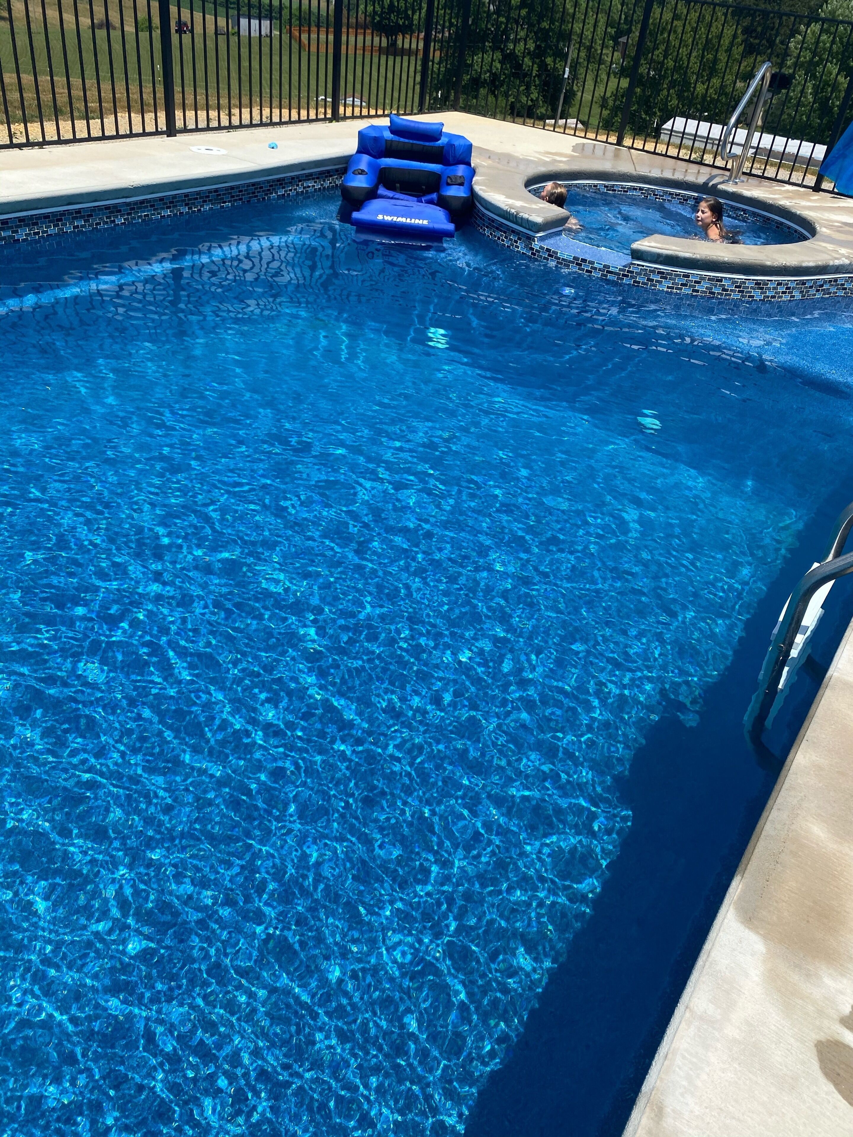 A clear blue swimming pool with a blue inflatable float and a small hot tub area.