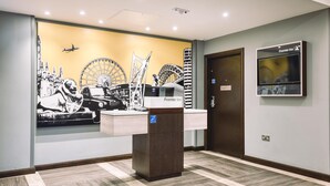 A hotel reception area with a check-in counter, a wall mural of a cityscape, and a Premier Inn sign. - Premier Inn London Sutton (Sutton)