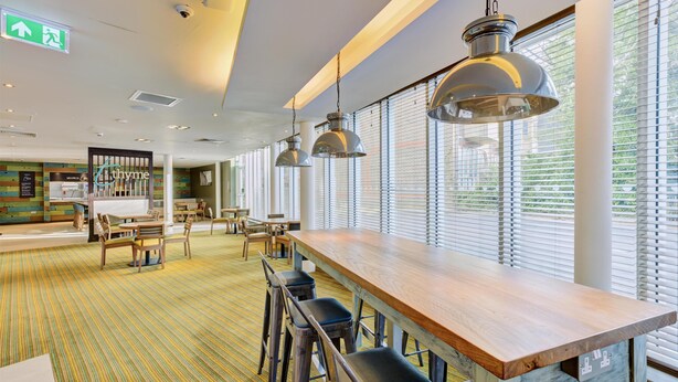 Um interior moderno com um longo balcão de madeira, várias luminárias pendentes e um tapete listrado.