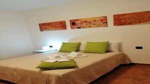 A neatly made bed with green and white pillows, a bedside table with a lamp, and three paintings on the wall. - "The Corte Giovanna" (Rescaldina)