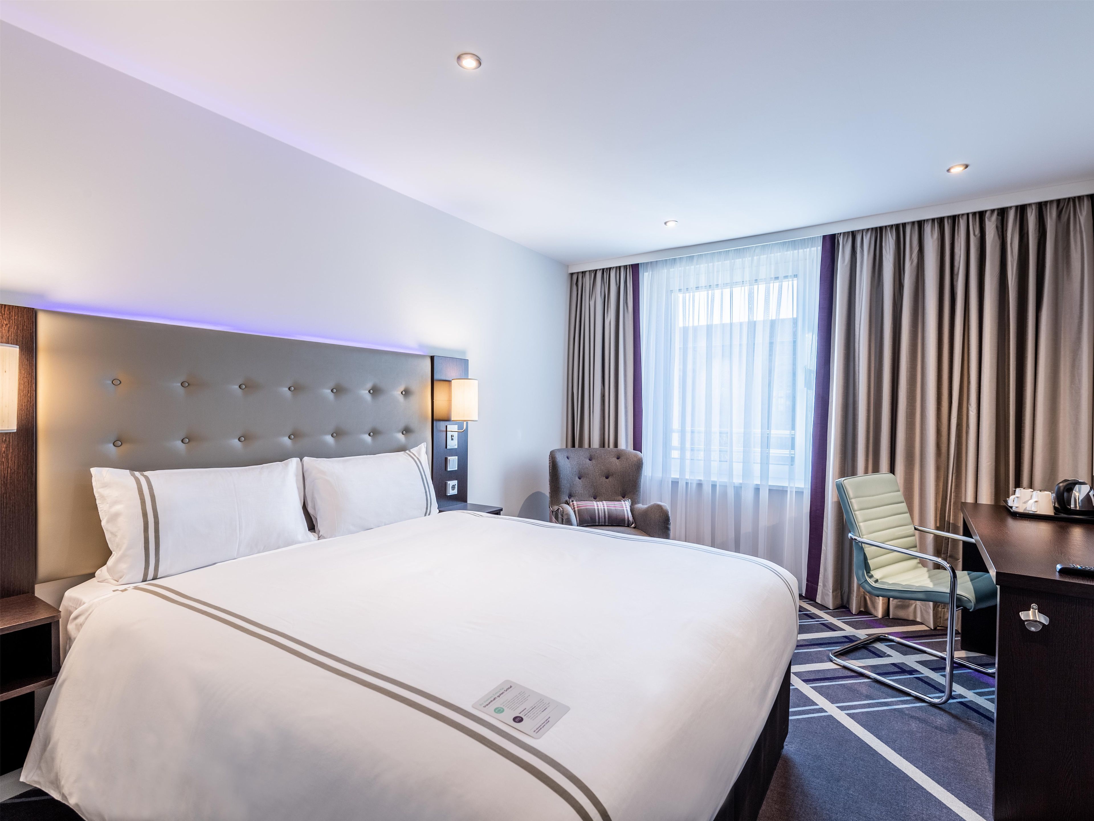 A hotel room with a large bed, a desk, a chair, and a window with curtains.