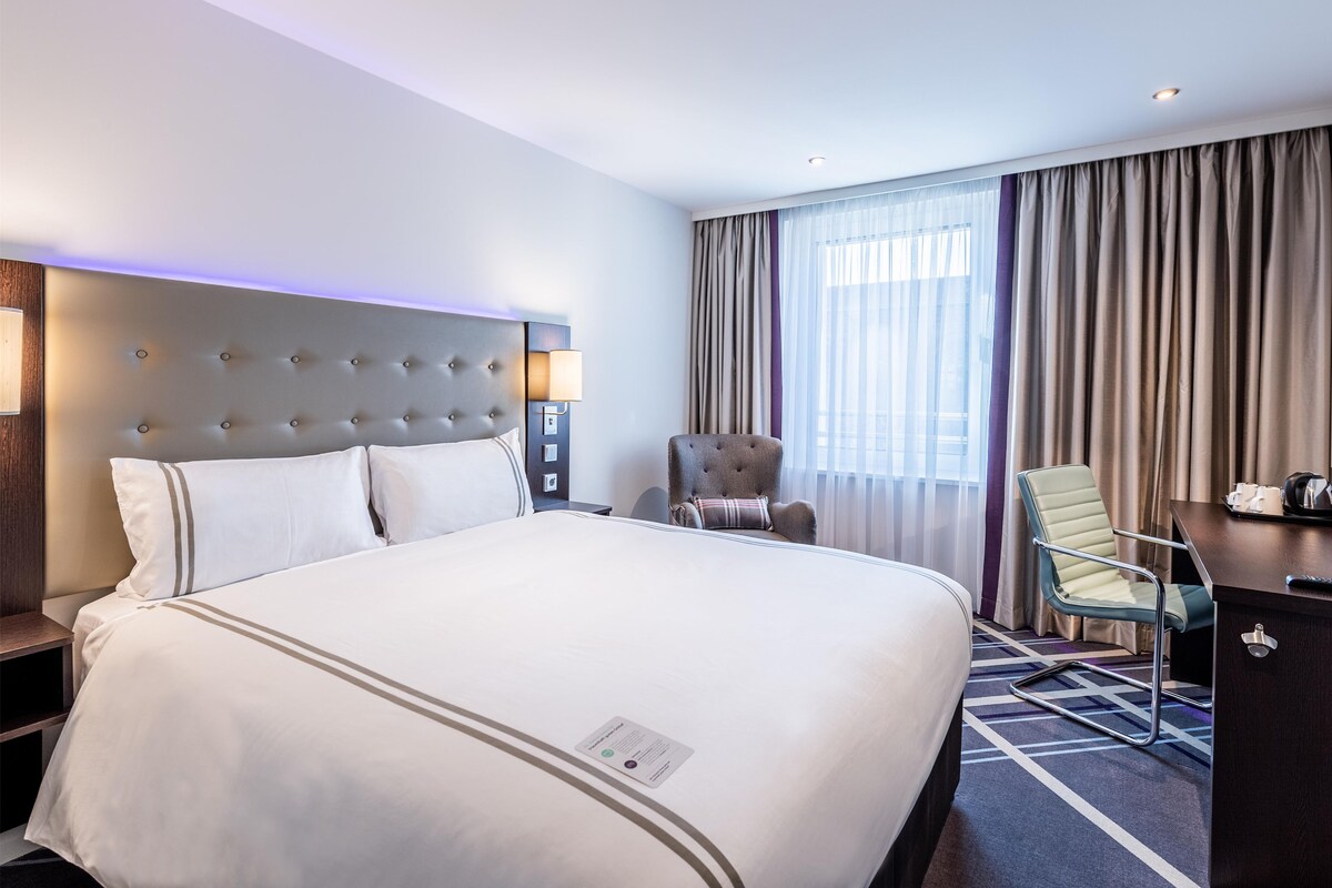 Habitación de hotel con una cama grande, un escritorio, una silla y una ventana con cortinas.