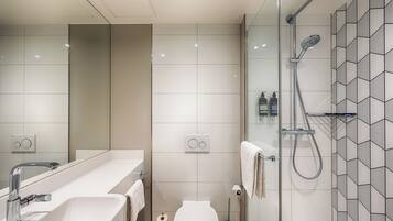 Un baño moderno con ducha acristalada, lavabo blanco y retrete.