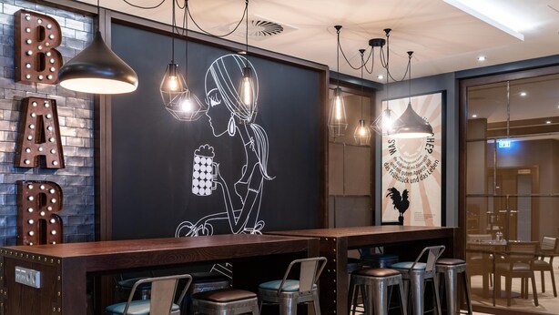 Zona de bar con un mural, lámparas colgantes y taburetes.