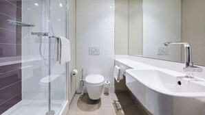 Un baño moderno con cabina de ducha de vidrio, un inodoro blanco y un lavamanos grande de color blanco con un espejo.
