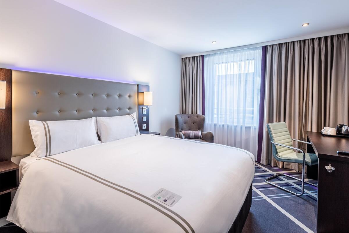 A hotel room with a large bed, a desk, a chair, and a window with curtains.