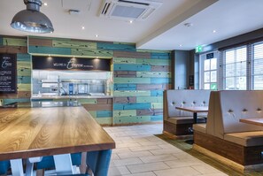 A restaurant interior with a wooden table and booth seating, a menu board, and a wall with a wood plank pattern. - Premier Inn Marlborough (Marlborough)