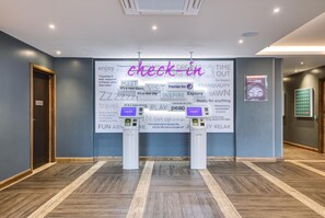 A hotel lobby with a check-in counter, a digital kiosk, and a wall with motivational quotes and travel-related phrases. - Premier Inn Marlborough (Marlborough)