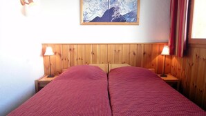 Cama doble con colcha de lunares rojos, cabecera de madera, dos mesitas de noche con lámparas y un cuadro en la pared.