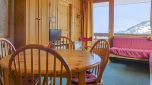 A wooden cabin interior with a dining table, chairs, a television, and a sofa by a window with a mountain view. - 10m from ski slopes, 1st floor, balcony, 33m², Méribel-Mottaret (Méribel - Les Allues)