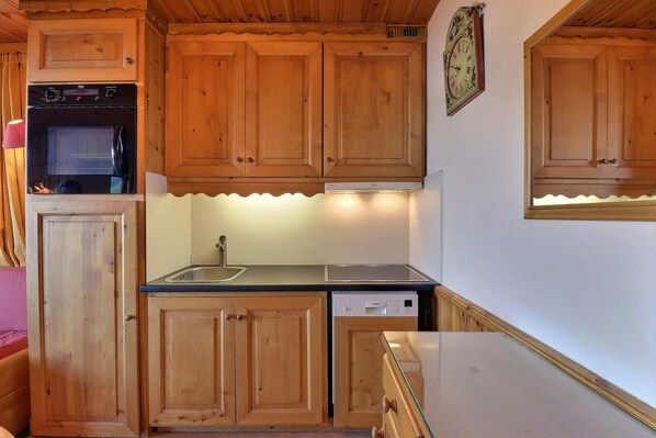 A compact kitchen with wooden cabinets, a built-in oven, a sink, and a dishwasher.