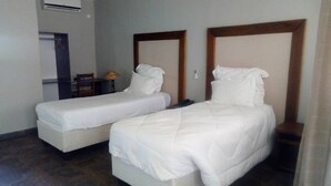 A hotel room with two single beds, a small table, and an air conditioning unit. - Pakali Lodges (Livingstone)
