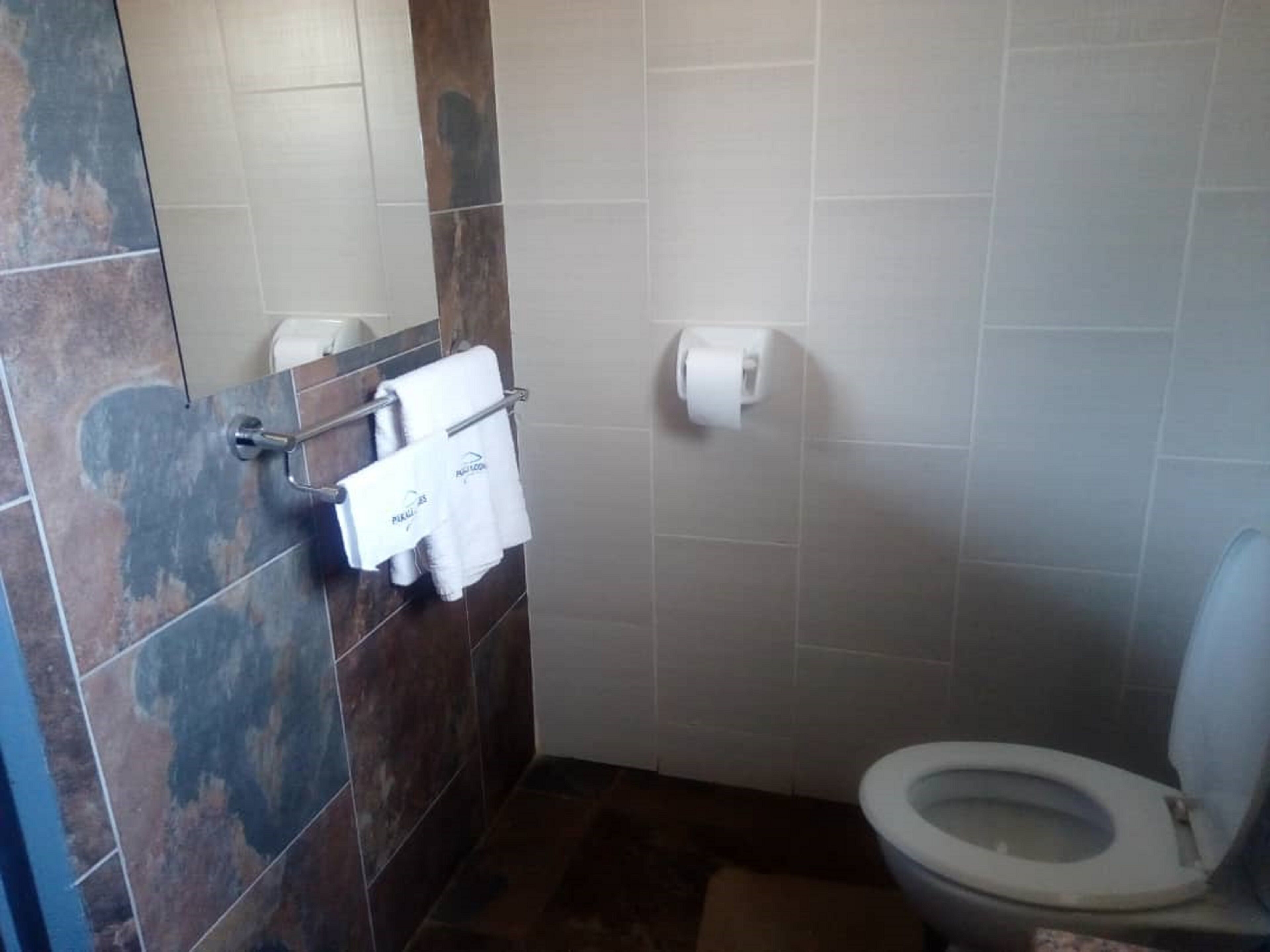 Un baño con inodoro, un perchero con toalla blanca y dispensador de toallas de papel.