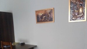 A small room with a wooden desk, a chair, a white refrigerator, and two framed artworks on the wall. - Pakali Lodges (Livingstone)