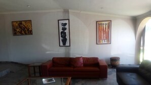 A living room with a red sofa, a black sofa, and a glass coffee table. There are three framed artworks on the walls. - Pakali Lodges (Livingstone)