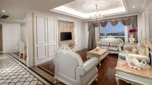 A luxurious living room with a high ceiling, ornate ceiling design, a large window with curtains, and a city view.