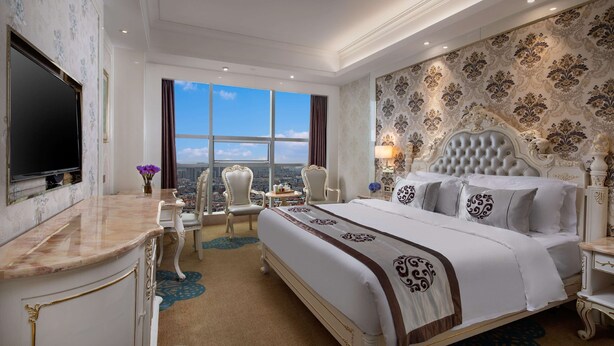A luxurious hotel room with a large bed, a television, a desk, and a view of the city.