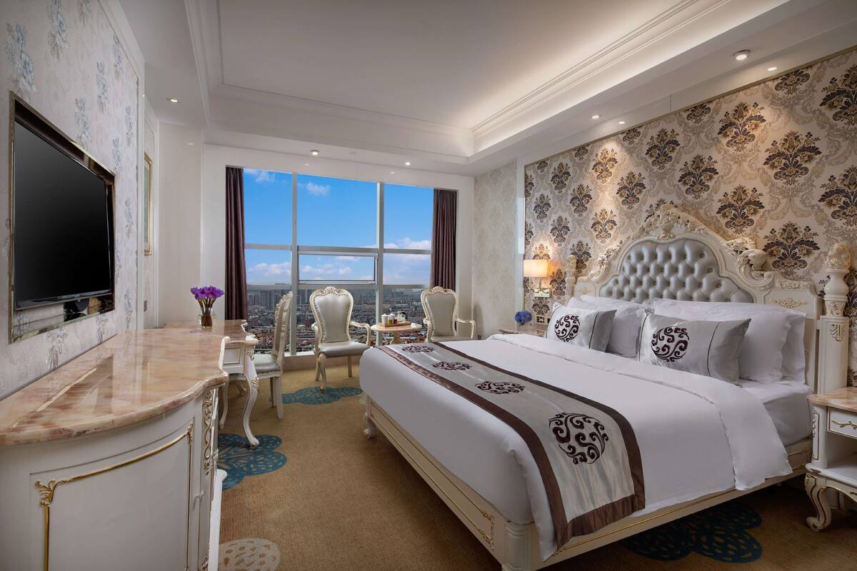 Ein luxuriöses Hotelzimmer mit einem großen Bett, Fernseher, Schreibtisch und Blick auf die Stadt.