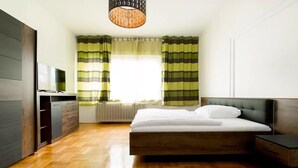 Un dormitorio moderno con suelo de madera, una cama con cabecera gris, una mesita de noche, un aparador y un televisor sobre un mueble.