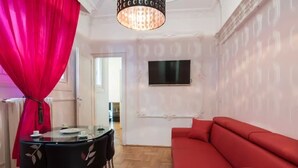 A room with a red sofa, a glass table with chairs, a TV mounted on the wall, and a patterned wallpaper. - Budapest Promenade with balcony (Budapest)