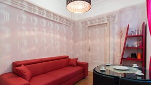 A red sofa, a glass table with chairs, and a red bookshelf with items on it. - Budapest Promenade with balcony (Budapest)