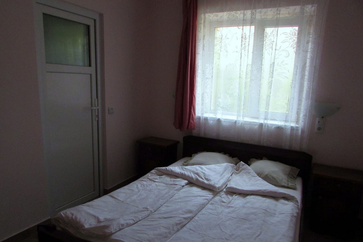 Une chambre à coucher comprenant un lit, une table de chevet, une armoire et une fenêtre avec des rideaux.